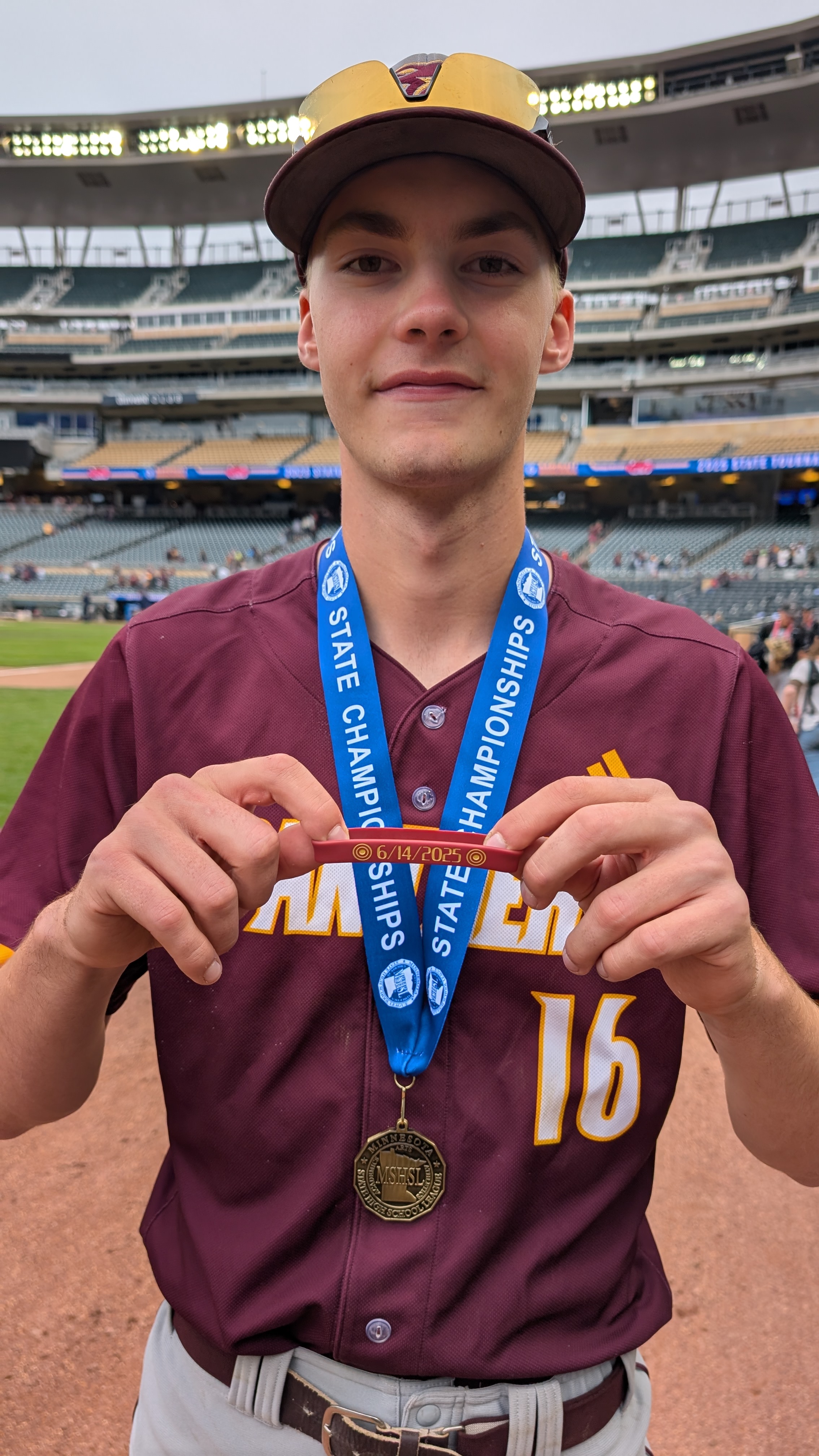 Pine Island Baseball player Lucas Sems holds up a wristband that reads "6/14/2025" with a pair of target icons.