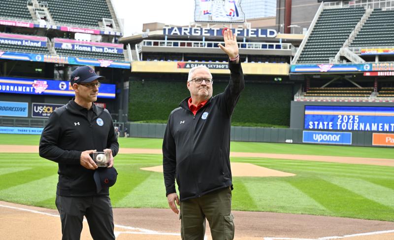 John Millea waves to the crowd at Target Field during a Baseball State Tournament pregame ceremony. Executive Director MSHSL Executive Director Erich Martens stands next to him with a commemorative baseball and award.