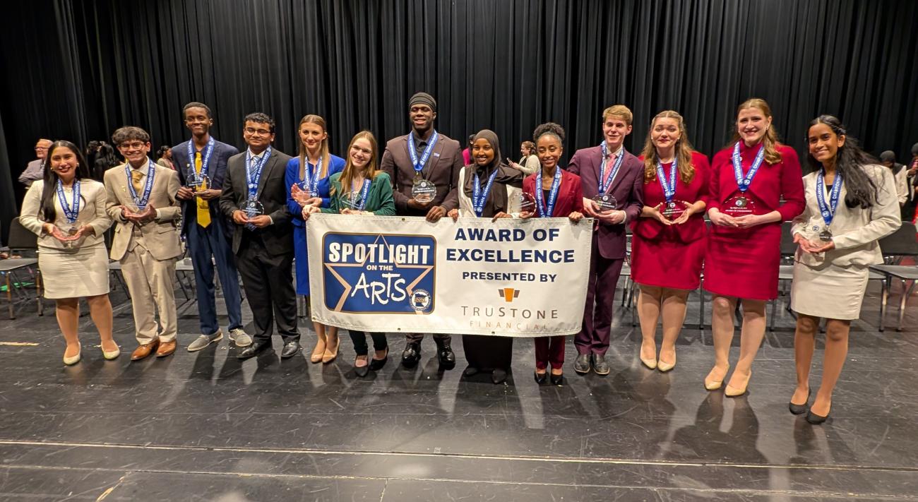 The 2025 Class AA Speech individual state champions holding a Spotlight on the Arts banner and their trophies.