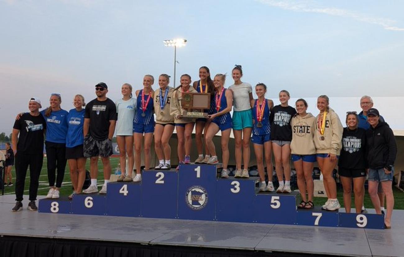 The Janesville-Waldorf-Pemberton Girls Track and Field team on the MSHSL podium with first-place trophy.