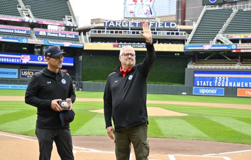 John Millea waves to the crowd at Target Field during a Baseball State Tournament pregame ceremony. Executive Director MSHSL Executive Director Erich Martens stands next to him with a commemorative baseball and award.
