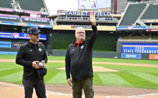 John Millea waves to the crowd at Target Field during a Baseball State Tournament pregame ceremony. Executive Director MSHSL Executive Director Erich Martens stands next to him with a commemorative baseball and award.
