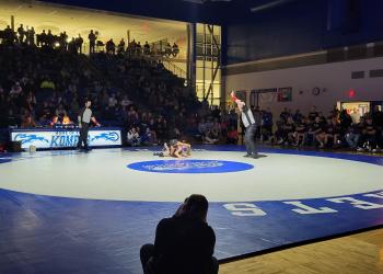 A spotlight shines on the Kasson-Mantorville mat during a high school wrestling match.