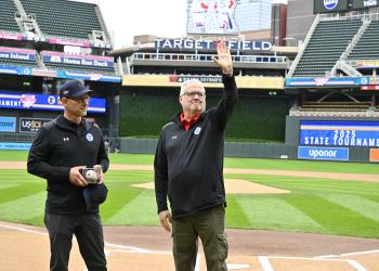 John Millea waves to the crowd at Target Field during a Baseball State Tournament pregame ceremony. Executive Director MSHSL Executive Director Erich Martens stands next to him with a commemorative baseball and award.